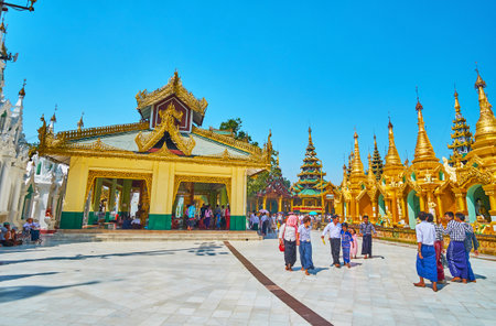 YANGON, MYANMAR - FEBRUARY 27, 2018:  Shwedagon Zedi Daw with line of golden stupas and shady...