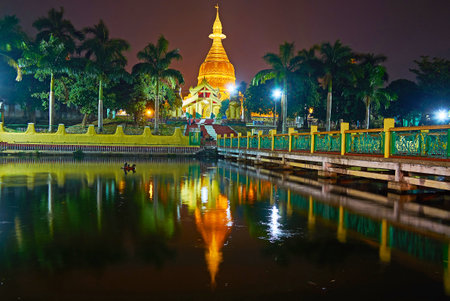 The evening walk at the ponds of Mahavijaya Pagoda with  view on garden, golden stupa and its reflection in black waters, Yangon, Myanmar.のeditorial素材