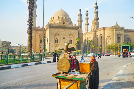 CAIRO, EGYPT - DECEMBER 21, 2017: Merchants push the food cart with oven on top, walking along Saladin Square, with a view on Sultan Hassan and the Royal (Al-Rifai') Mosques, on December 21 in Cairo.のeditorial素材