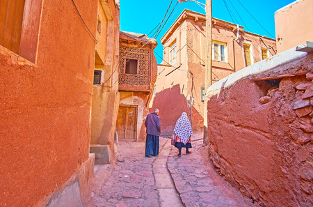 The senior couple in traditional Abyanaki clothes walks along the narrow ascent among the red adobe houses, Abyaneh, Iran.の写真素材