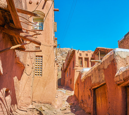 The narrow backstreet, lined with old houses, covered with red clay and located on the slope of Karkas mountain, Abyaneh, Iran.の写真素材