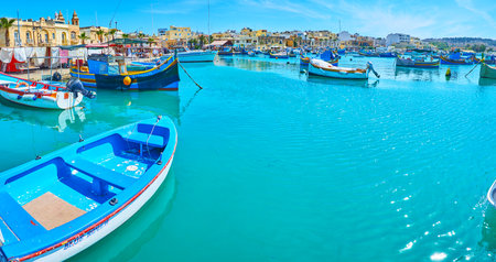 MARSAXLOKK, MALTA - JUNE 18, 2018: Walk along the seaside promenade of the village with a view on boats in harbour and hills of Delimara peninsula on background, on June 18 in Marsaxlokkのeditorial素材