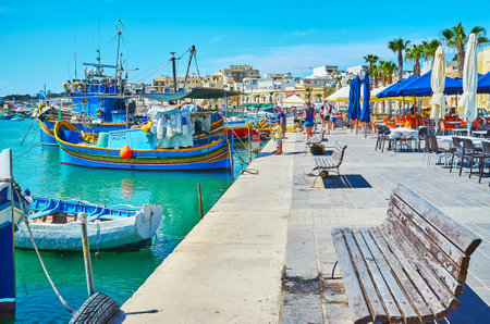 MARSAXLOKK, MALTA - JUNE 18, 2018: The harbour of fishing village with traditional luzzu boats among the ordinary vessels, cozy cafes and tourist stalls along the shore, on June 18 in Marsaxlokk.のeditorial素材