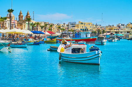 MARSAXLOKK, MALTA - JUNE 18, 2018: The coastline of the village is occupied with residential quarters, historic edifices, tourist market and cafes, on June 18 in Marsaxlokkのeditorial素材
