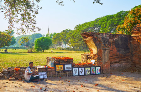 AVA, MYANMAR - FEBRUARY 21, 2018: The painter demonstrates his artworks on territory of Yadana Hsemee Pagoda under the red silk-cotton tree, on February 21 in Ava.のeditorial素材