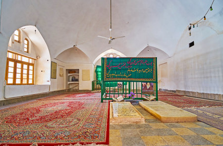 YAZD, IRAN - OCTOBER 18, 2017: The modest interior of the mausoleum in Jameh Mosque, the tombstones are surrounded with colorful Persian carpets, on October 18 in Yazd.のeditorial素材