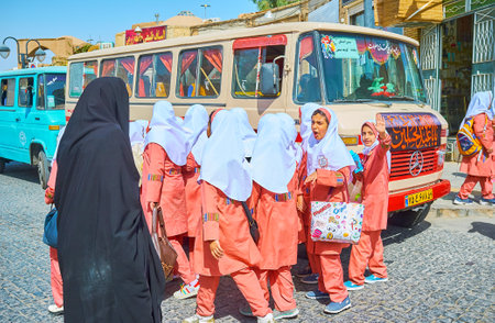 YAZD, IRAN - OCTOBER 18, 2017:  The schoolgirls in bright orange uniform at the school bus in old town, on October 18 in Yazd.のeditorial素材