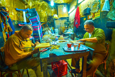 CAIRO, EGYPT - DECEMBER 20, 2017: Two carpenters in small workshop on historical El-Gamaleya street cut out the workpieces, depicting different religion signs and inscriptions, on December 20 in Cairo.のeditorial素材