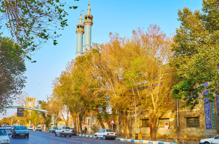 YAZD, IRAN - OCTOBER 18, 2017: The lush shady trees line Imam Khomeini street, the tall twin minarets of Rozeh Mohamadieh Mosque (Hazireh) are seen on the background, on October 18 in Yazdのeditorial素材