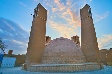The evening walk in old Yazd with a view on yakhchal (ice chamber) with tall wind towers (badgirs) and bright sunset sky on the background, Iran.の写真素材