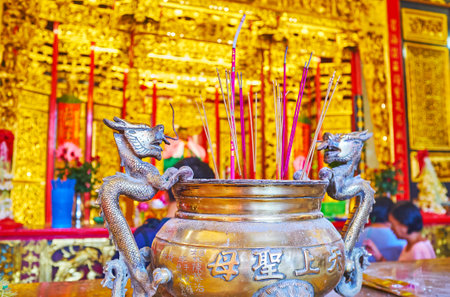 YANGON, MYANMAR - FEBRUARY 17, 2018:  The copper vase with incense sticks is decorated with Chinese inscriptions and dragons, Kheng Hock Keong (Qingfu) Temple, on February 17 in Yangon.のeditorial素材