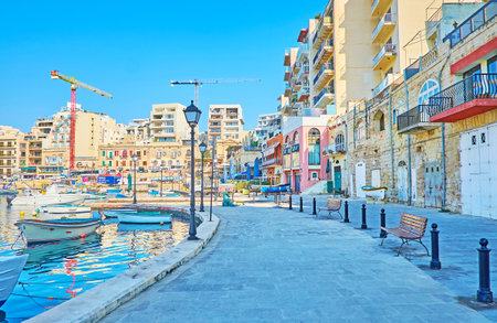 ST JULIANS, MALTA - JUNE 20, 2018: Enjoy the morning shade in seaside promenade at Spinola Bay with a view on fishing boats, tourist restaurants and modern neighborhoods, on June 20 in St Julians.のeditorial素材