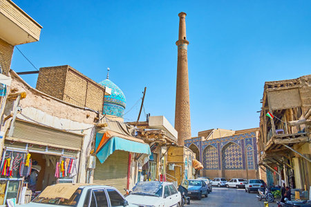 ISFAHAN, IRAN - OCTOBER 21, 2017: The shabby street of Grand (Qeysarie, Soltani) Bazaar with stalls and shops located in old huts and tall minaret of Ali Mosque on the background, on October 21 in Isfahan.のeditorial素材