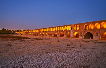 Evening walk along the bank of dried up Zayanderud river with a view on brightly illuminated historic Siosepol bridge, Isfahan, Iran.のeditorial素材