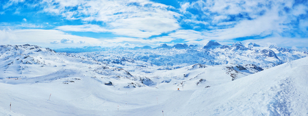 Fast changing clouds over the snowy slopes of Krippenstein mount with its numerous ski pistes and the sharp peaks of Dachstein massif on background, Obertraun, Salzkammergut, Austria.の写真素材