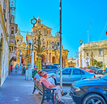 SIGGIEWI, MALTA - JUNE 16, 2018: The company of senior Maltese man sits on the bench in front of the St Nicholas Church, on June 16 in Siggiewiのeditorial素材