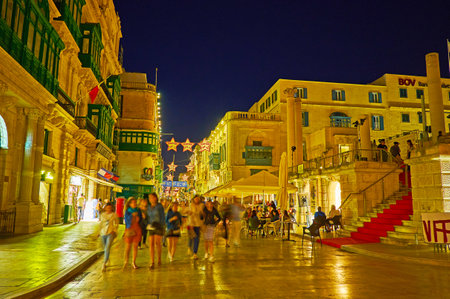 VALLETTA, MALTA - JUNE 16, 2018: The crowded evening Republic street with outdoor cafes, souvenir stores, site of ruined Opera House and historic mansions, on June 16 in Valletta.のeditorial素材