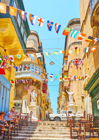 VALLETTA, MALTA - JUNE 19, 2018: The colorful flag garlands flutter in the wind above the narrow street of St Lucia, on June 19 in Vallettaのeditorial素材