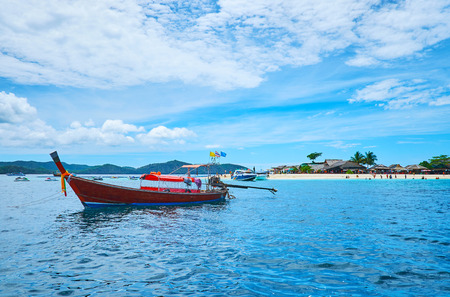 The bright red long-tail boat is moored next to the sandy shore of Khai Nok island, Phuket, Thailandの写真素材