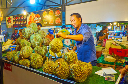 AO NANG, THAILAND - APRIL 27, 2019: The stall of Ao Nang Night Market with heap of durians, the merchant checks the fruits' ripeness, knocking their thorny rind with a stick, on April 27 in Ao Nangのeditorial素材