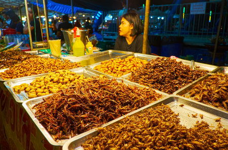 AO NANG, THAILAND - APRIL 27, 2019: The stall of Ao Nang Night Bazaar with extreme snacks - fried bamboo worms, crickets, grasshoppers, water bugs and silk worms, on April 27 in Ao Nangのeditorial素材