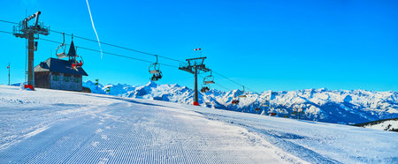 Panorama of Schmittenhohe mountain top with perfect corduroy ski piste, Kapellenbahn chairlift, small Elisabeth chapel and Alpine range on background, Zell am See, Austriaのeditorial素材