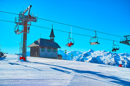 Kapellenbahn ski lift running on Schmittenhohe mount with a view on wooden Elisabeth chapel, sportsmen and snowy Alps, Zell am See, Austriaのeditorial素材