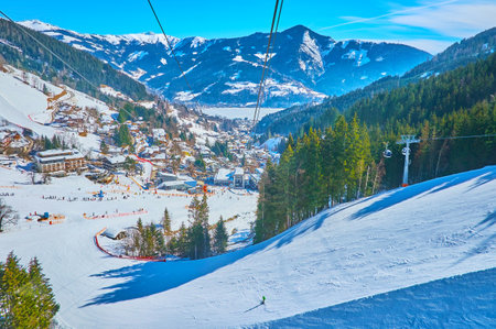 Aerial view on curved ski pistes, stretching along the snowy slope of Schmitten mount, lush coniferous forests and Zeller see valley with fozen lake at mountain foot, Zell am See, Austriaのeditorial素材