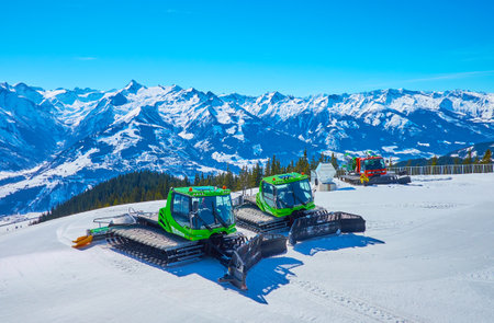 ZELL AM SEE, AUSTRIA - FEBRUARY 28, 2019: Parked snow grooming vehicles on the slope of Schmitten mount with scenic Alpine scenery and Kitzsteinhorn mountain on background, on February 28 in Zell am Seeのeditorial素材