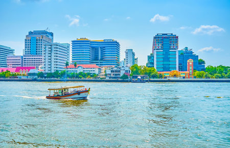 The small wooden motor boat sails on Chao Phraya, along modern buildings of Bangkok, Thailandのeditorial素材