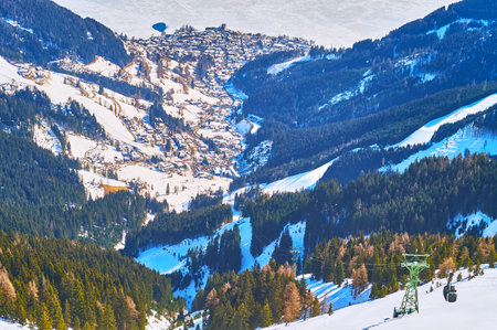 The peak of Schmitten mount overlooks the Zeller see valley with houses on the bank of frozen lake and snowy Alpine slopes around it, Zell am See, Austria.のeditorial素材