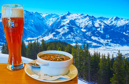 ZELL AM SEE, AUSTRIA - FEBRUARY 28, 2019: Enjoy the dinner with sliced pancake soup and beer in cafe, located on Schmitten mountain slope and overlooking Kitzsteinhorn mount of Kaprun, on February 28 in Zell am Seeのeditorial素材