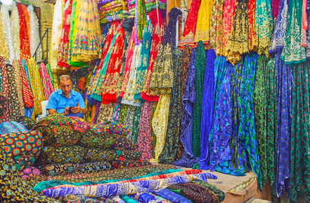 SHIRAZ, IRAN - OCTOBER 14, 2017: The merchant in textile stall of Vakil Bazaar among colorful fabrics, decorated with patterns, embroideries and lurex, on October 14 in Shiraz.のeditorial素材