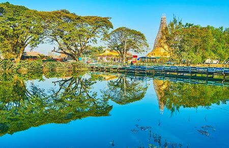 The pleasant walk by the Tharzi pond, surrounded by greenery, that hides golden pagoda of Buddhist Temple, Nyaungshwe, Myanmarの写真素材
