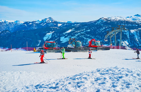 GOSAU, AUSTRIA - FEBRUARY 26, 2019: The skiers skate along the slope of Zwieselalm mount with a view on parked snow groomers and peaks of Dachstein West Alps, on February 26 in Gosau.のeditorial素材