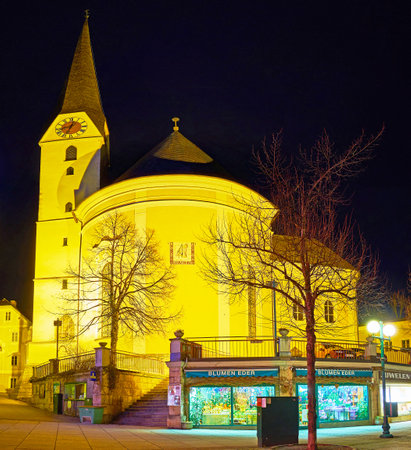 BAD ISCHL, AUSTRIA - FEBRUARY 20, 2019: The apse and tall clock tower of  St Nicholas Parish Church in evening lights with flower shop on the foreground, on February 20 in Bad Ischlのeditorial素材