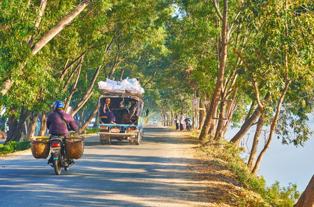NYAUNGSHWE, MYANMAR - FEBRUARY 20, 2018: The traffic along the intercity road with green trees on...
