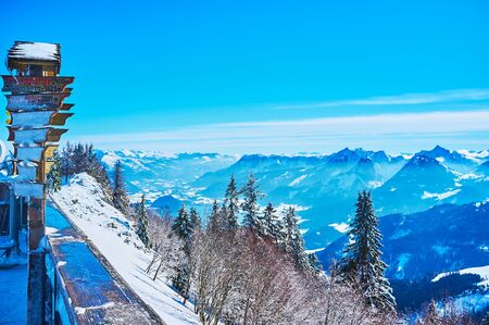 Watch spectacular Alpine landscape, covered with snow and surrounded by light haze, from the viewpoint of Zwolferhorn mount with vintage hiking frozen signboard, St Gilden, Salzkammergut, Austriaの写真素材