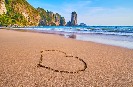 The painted heart on the wet sand of Monkey beach with a view on scenic rocks on the background, Ao Nang, Krabi, Thailandの写真素材