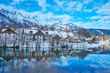 The snowbound housing of Bad Goisern is reflected on mirror surface of Traun river, Salzkammergut,...