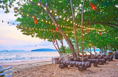 The scenic beach cafe is located in shade of tall spread trees, decorated with lamps and lanterns, Ao Nang, Krabi, Thailandの写真素材