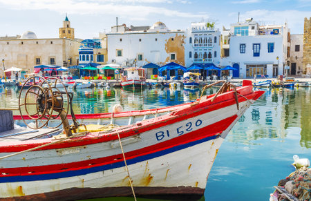 BIZERTE, TUNISIA - SEPTEMBER 4, 2015: Watch the shabby housing in port f Bizerte with old wooden fishing boat on the foreground, on September 4 in Bizerteのeditorial素材
