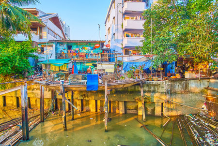 BANGKOK, THAILAND - APRIL 24, 2019: The shabby residential house with canoe on the piles above dirty Bang Lamphu canal in confluence with Chao Phraya river, on April 24 in Bangkokのeditorial素材