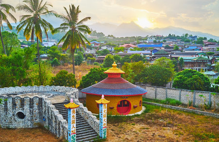 SANTICHON, THAILAND - MAY 5, 2019: The landscape of Chinese Yunnan cultural village with mountain silhouette on the background, lush palms, small houses and buildings of the fortress on the foreground, on May 5 in Santichonのeditorial素材