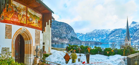 HALLSTATT, AUSTRIA - FEBRUARY 25, 2019: Panorama of the cemetery of Maria Am Berg Parish Church with a view on church's entrance with frescoes, Hallstattersee lake and snowy Alps on background, on February 25 in Hallstattのeditorial素材