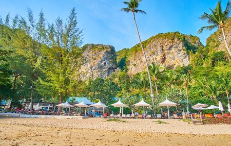 AO NANG, THAILAND - APRIL 25, 2019: The line of sunbeds with umbrellas at the lush green garden of Centara Grand beach, surrounded by huge rocks, on April 25 in Ao Nangのeditorial素材