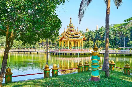 The view on small Buddhist shrine on the lake throught the lush trees on the bank in Theingottara park, Yangon, Myanmarの写真素材