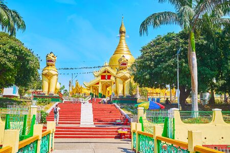 The giant chinthe lion guardians sit at the entrance to Mahavijaya (Maha Wizaya) Pagoda with ornate gate and huge golden stupa, Yangon, Myanmarの写真素材