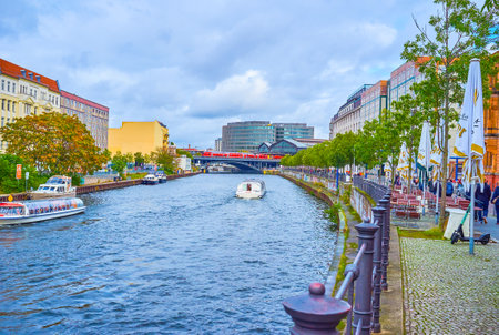 BERLIN, GERMANY - OCTOBER 3, 2019: The pleasant walk in the promenade of Spree river with possibility of having a break in outdoor cafe right at the handrails of the embankment, on October 3 in Berlinのeditorial素材
