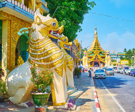 YANGON, MYANMAR - FEBRUARY 17, 2018: The gilt Chinthe lions of Yahandar Theindawgyi Temple face the Shwedagon Pagoda Road with heavy traffic and ornate South Gate of Shwedagon Zedi Daw on background, on February 17 in Yangon.のeditorial素材